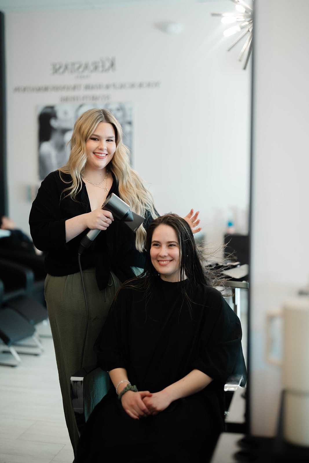 Hairdresser styling a client's hair at a salon, both smiling.