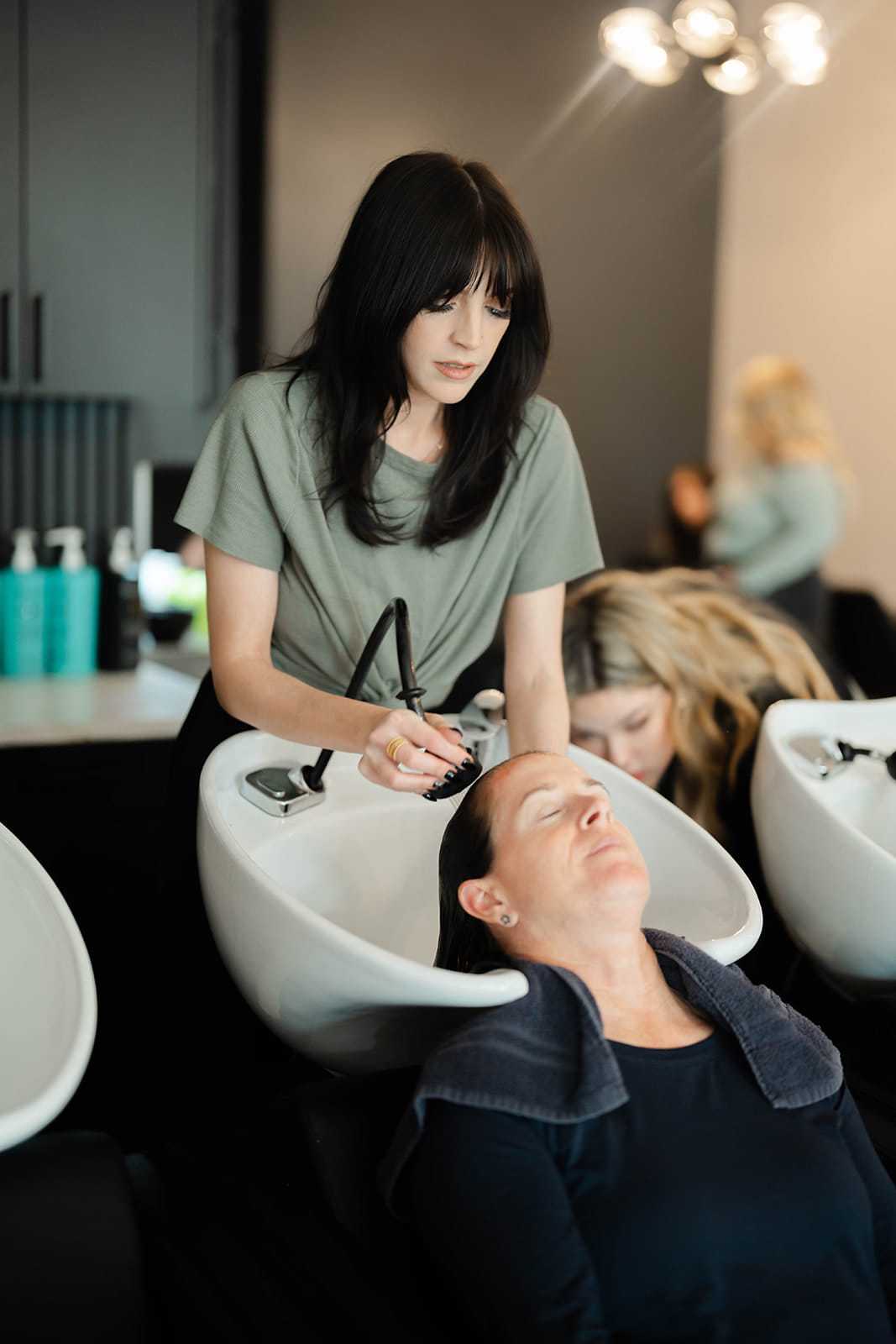 Hairstylist washing a client's hair at a salon sink.