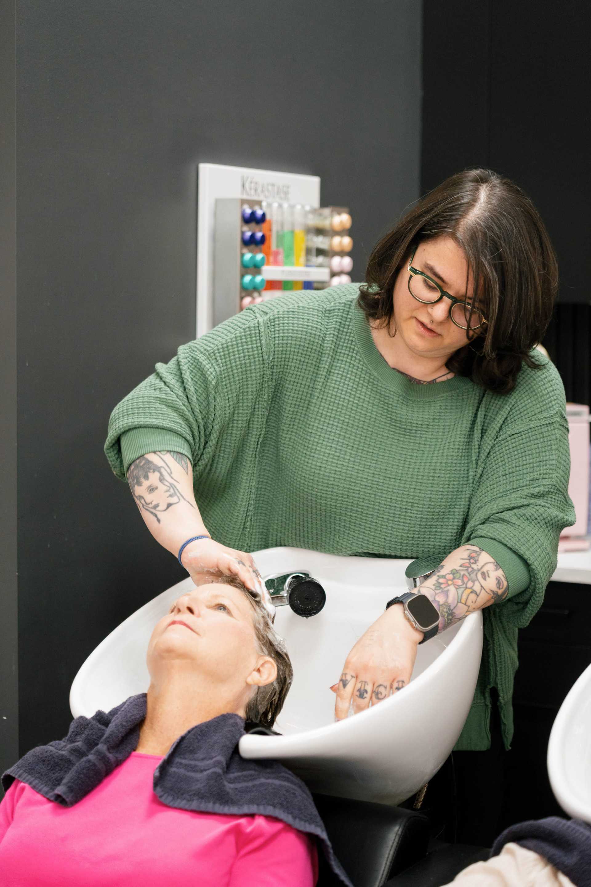 Hairdresser washing a woman's hair in a salon sink.