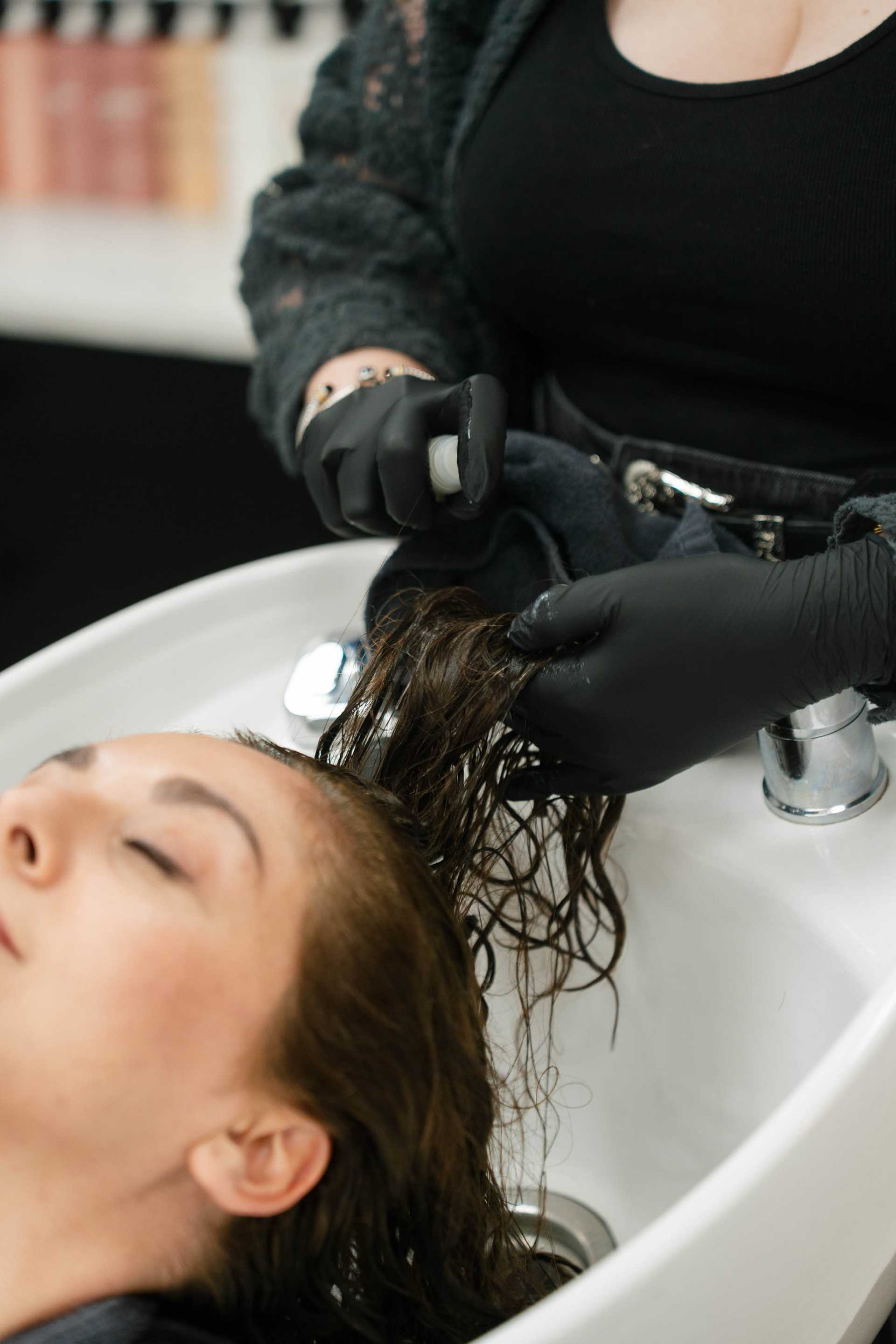 Woman getting hair washed at a salon sink by stylist with gloves.