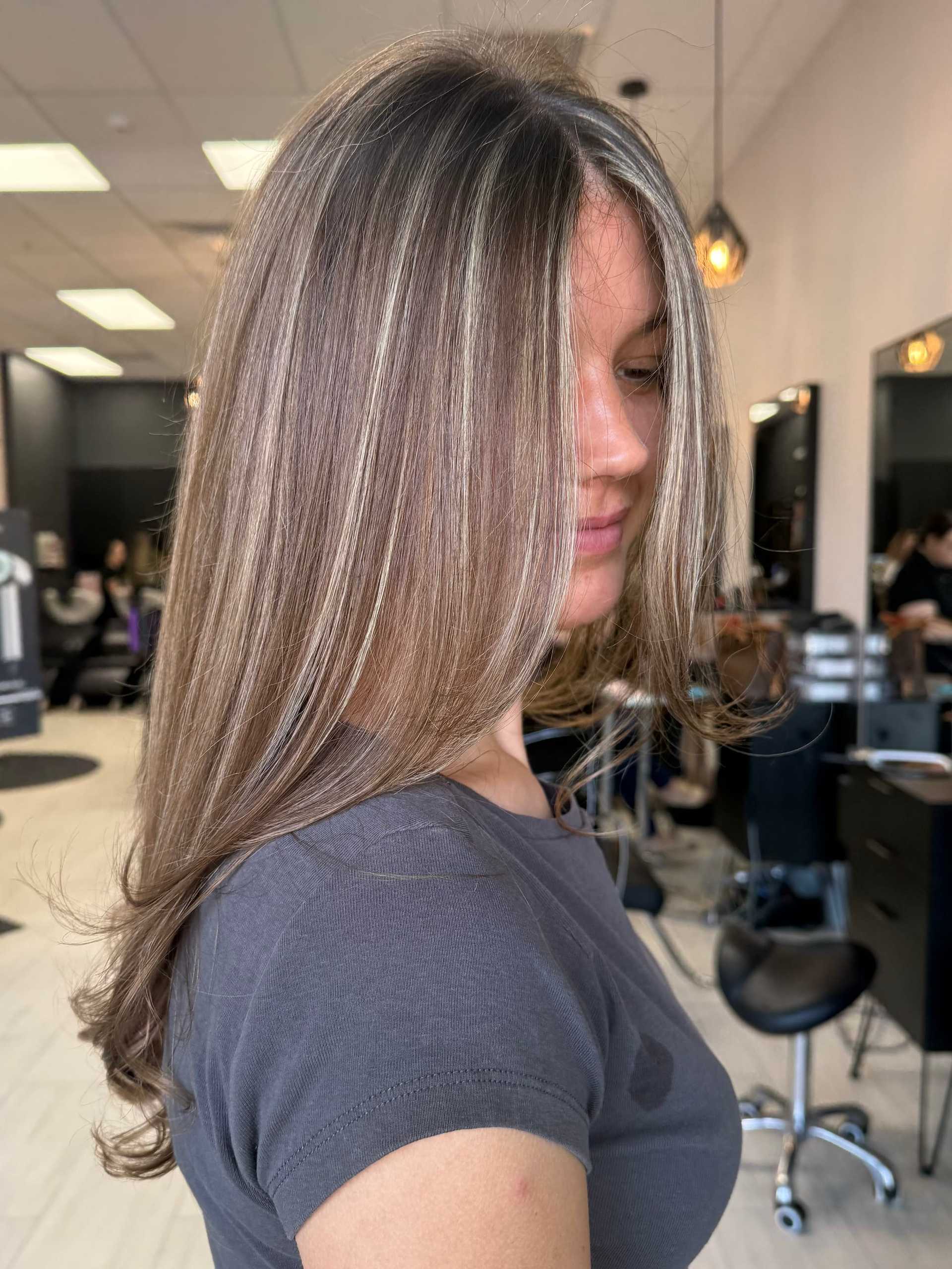 Woman with highlighted hair at a salon, sitting in front of styling stations.