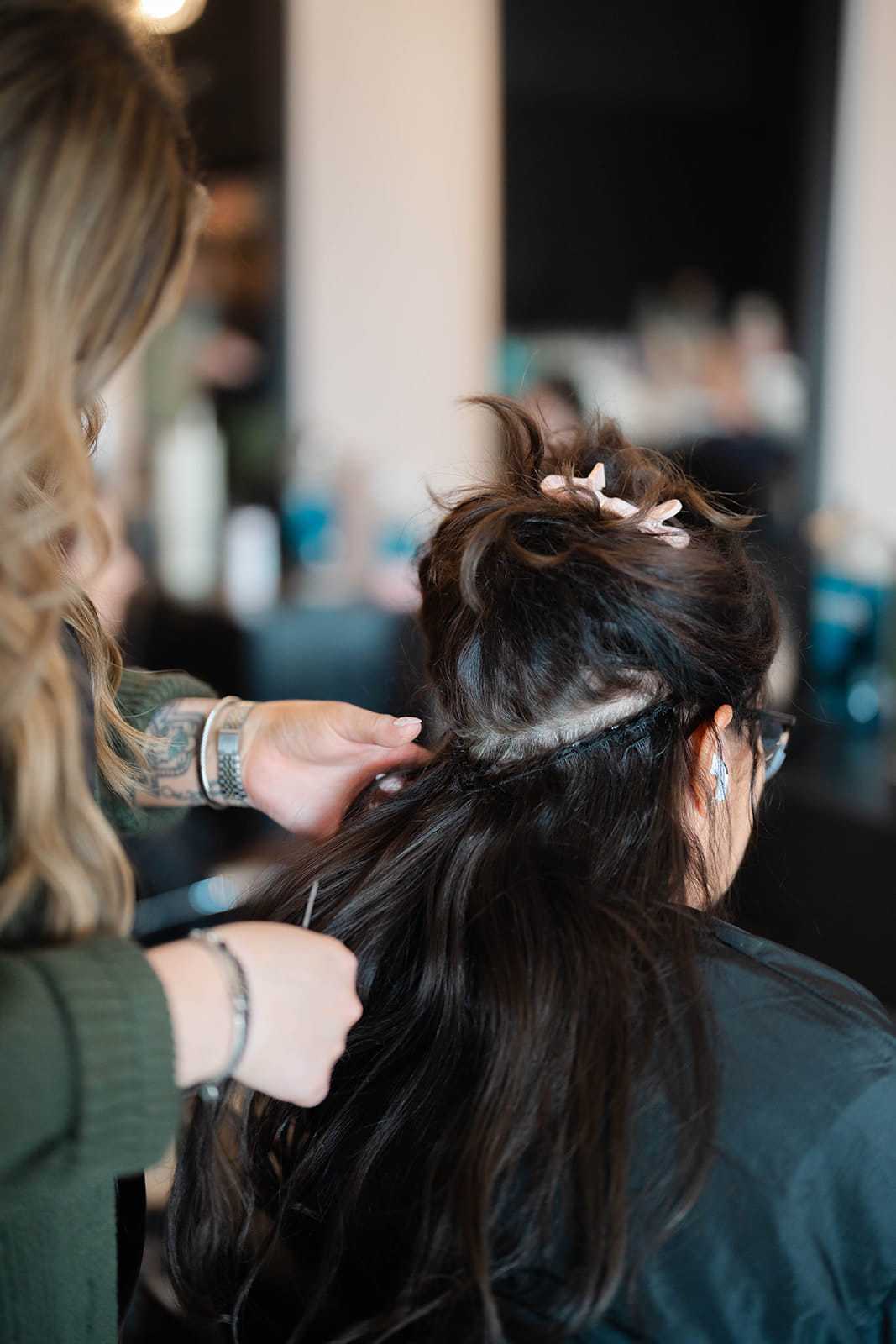 Hair stylist attaching hair extensions for a client in a salon setting.