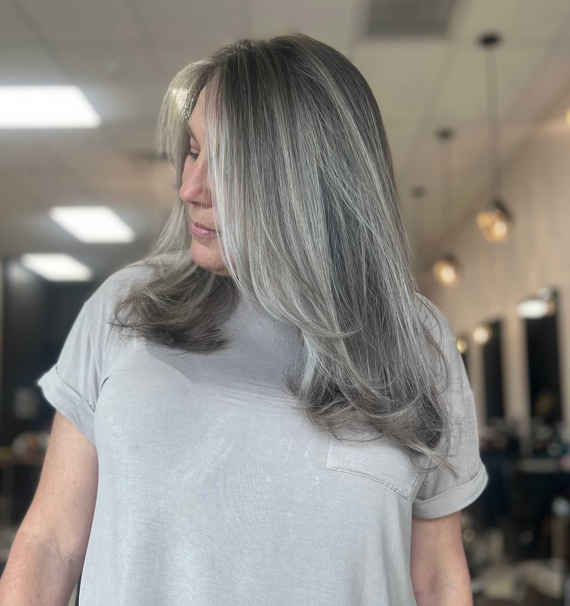 Woman with gray hair in salon, wearing a gray top, looking to the side.