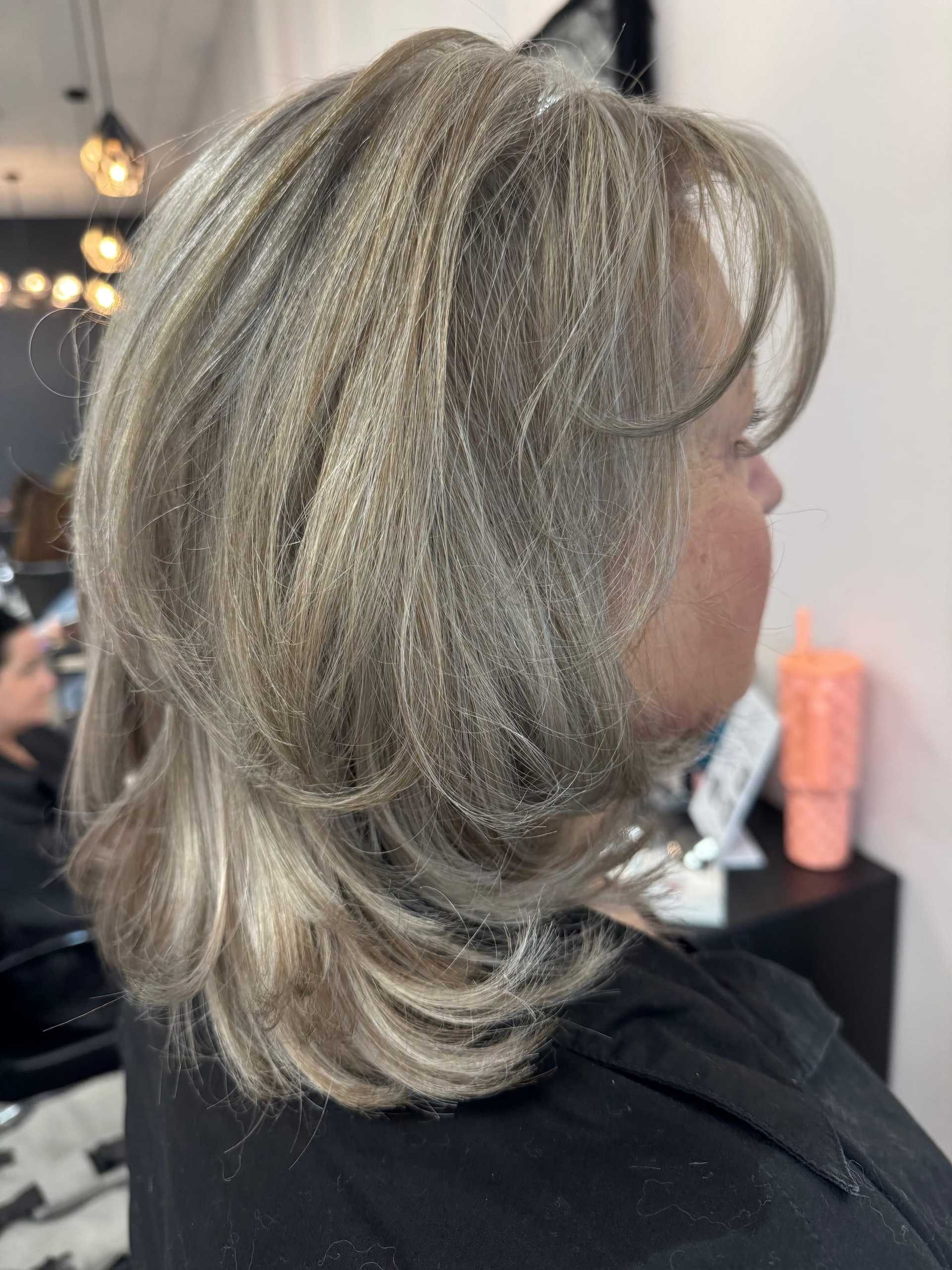 Short layered haircut with ash blonde highlights, side view in a salon setting.