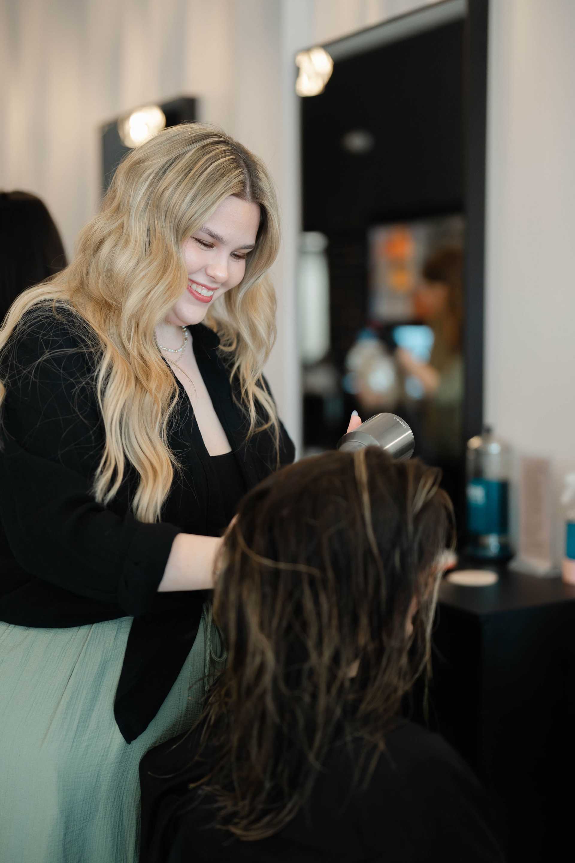 Hairdresser blow-drying a client's hair at a salon.