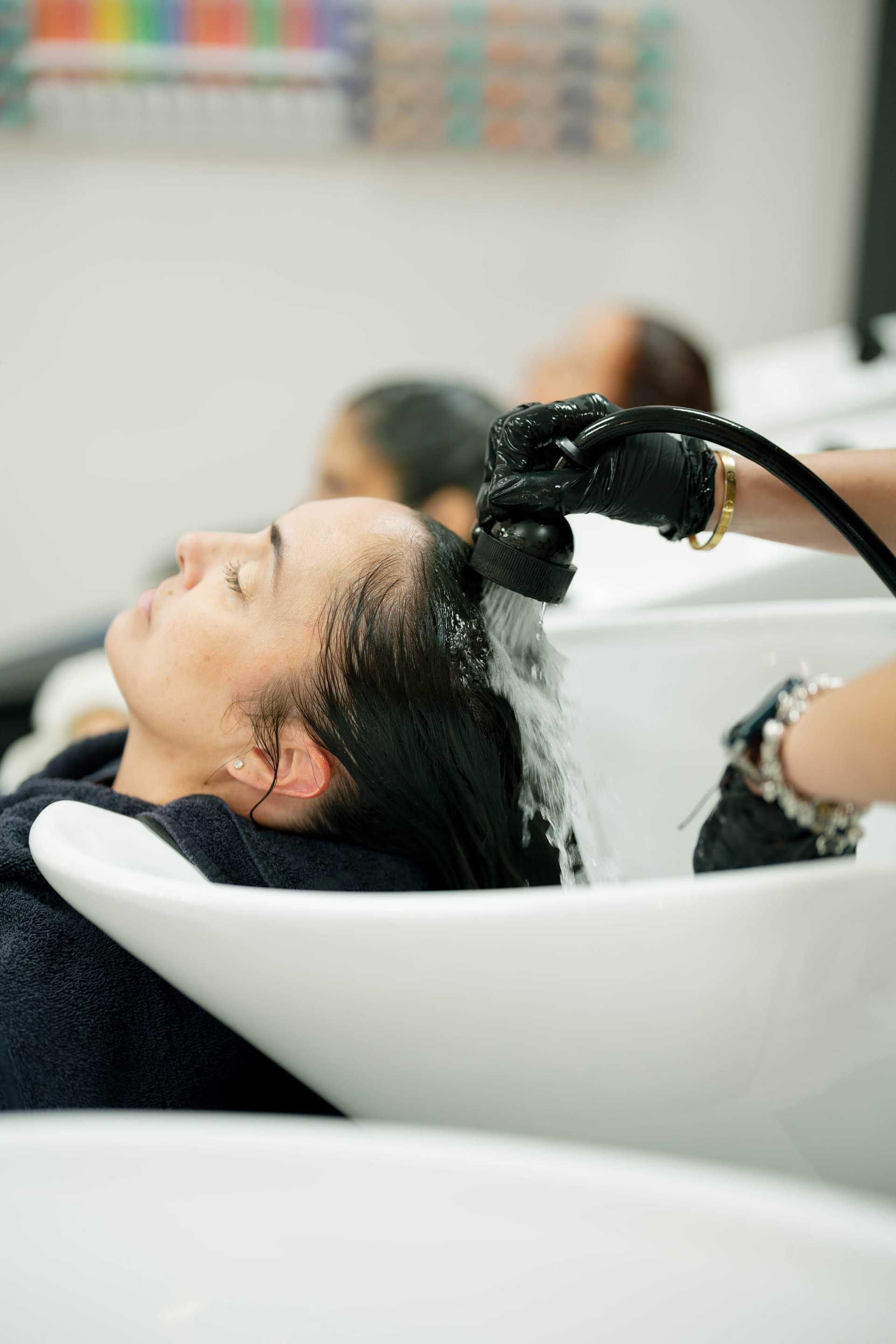 Client having their hair rinsed at a salon shampoo station during a professional hair treatment.