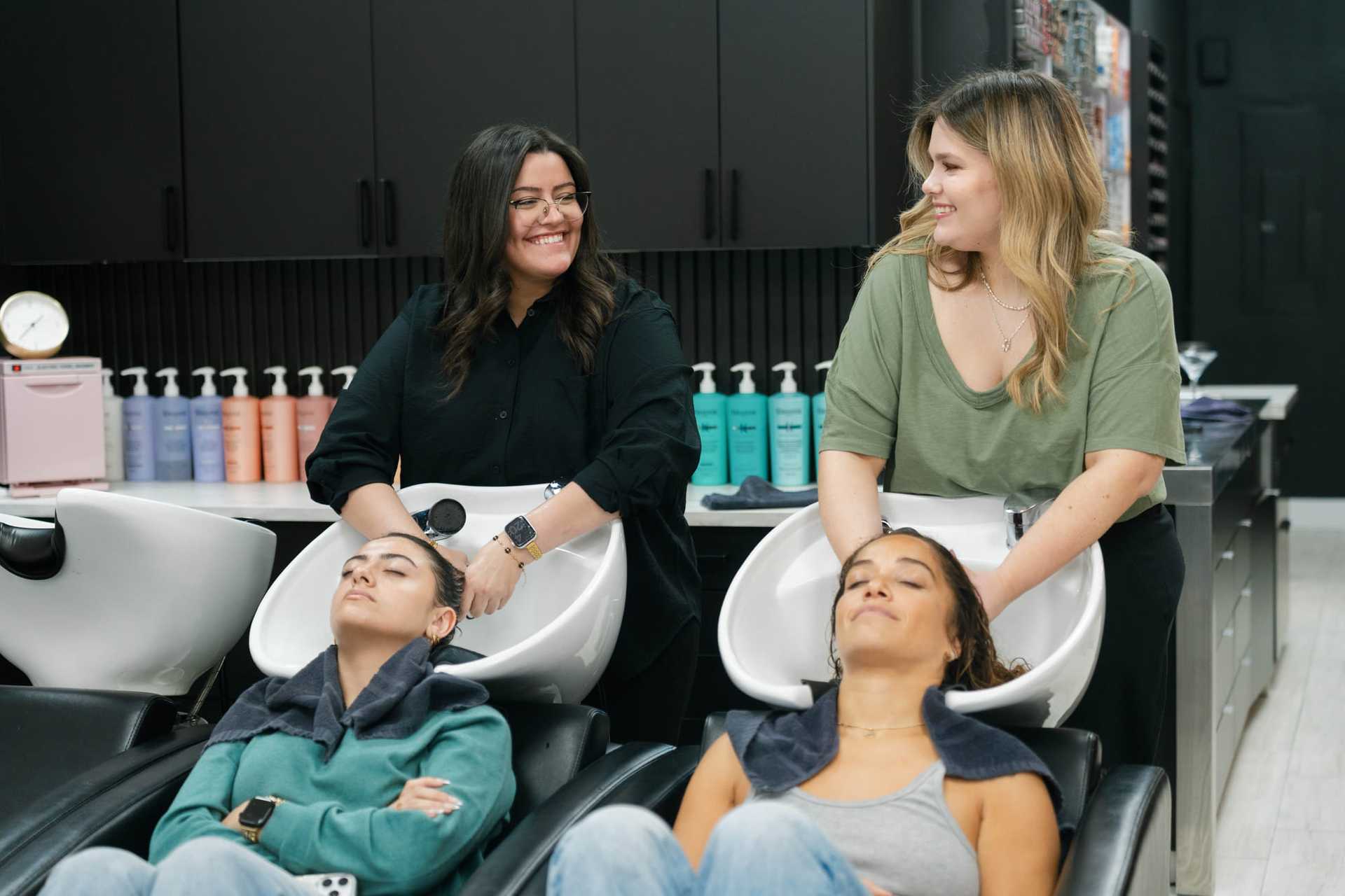 Women enjoying hair washing at salon, stylists smiling and chatting.