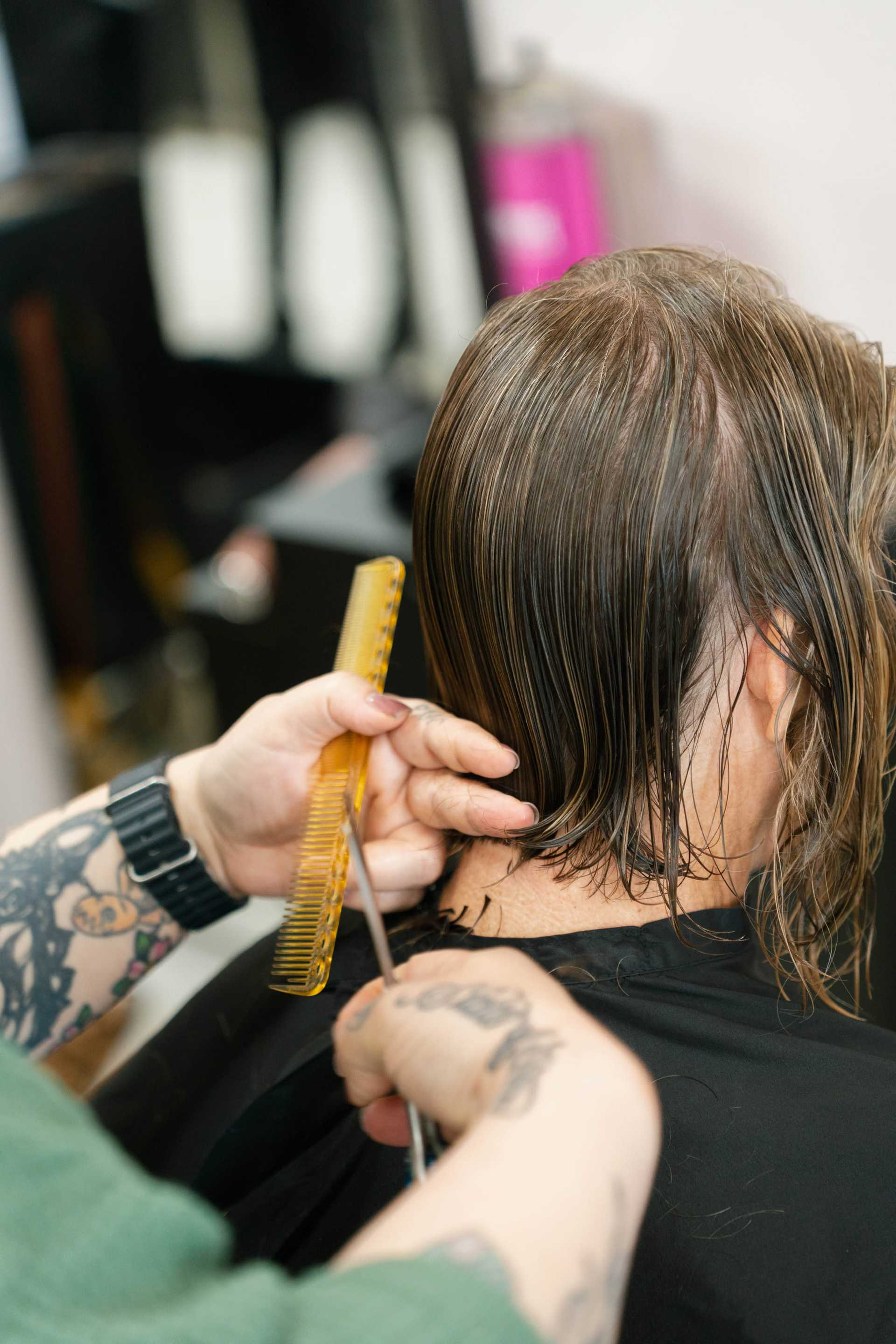 Haircut in progress at a salon, close-up of hands with scissors and comb.
