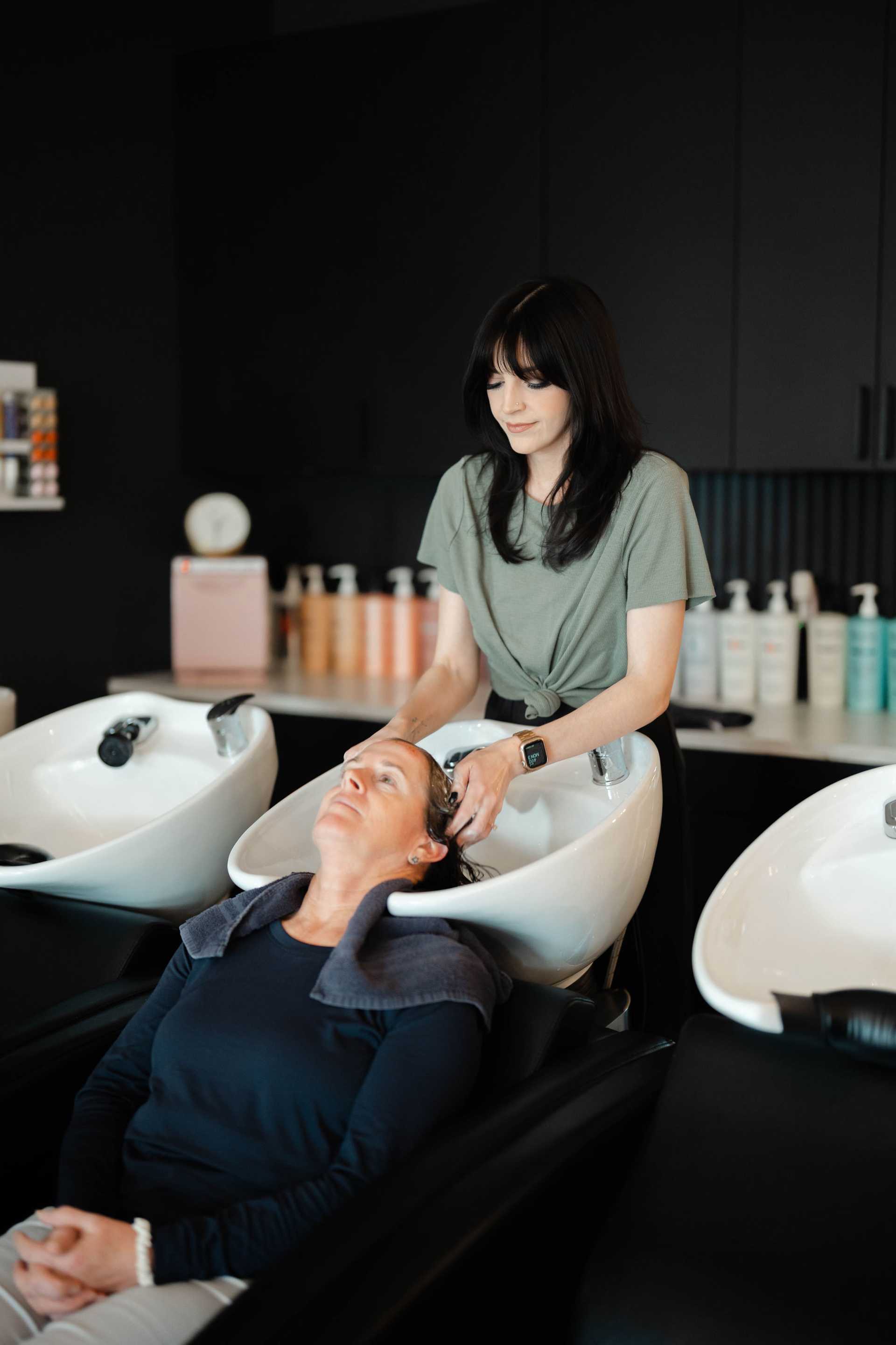 Hair stylist washing client's hair at salon sink.