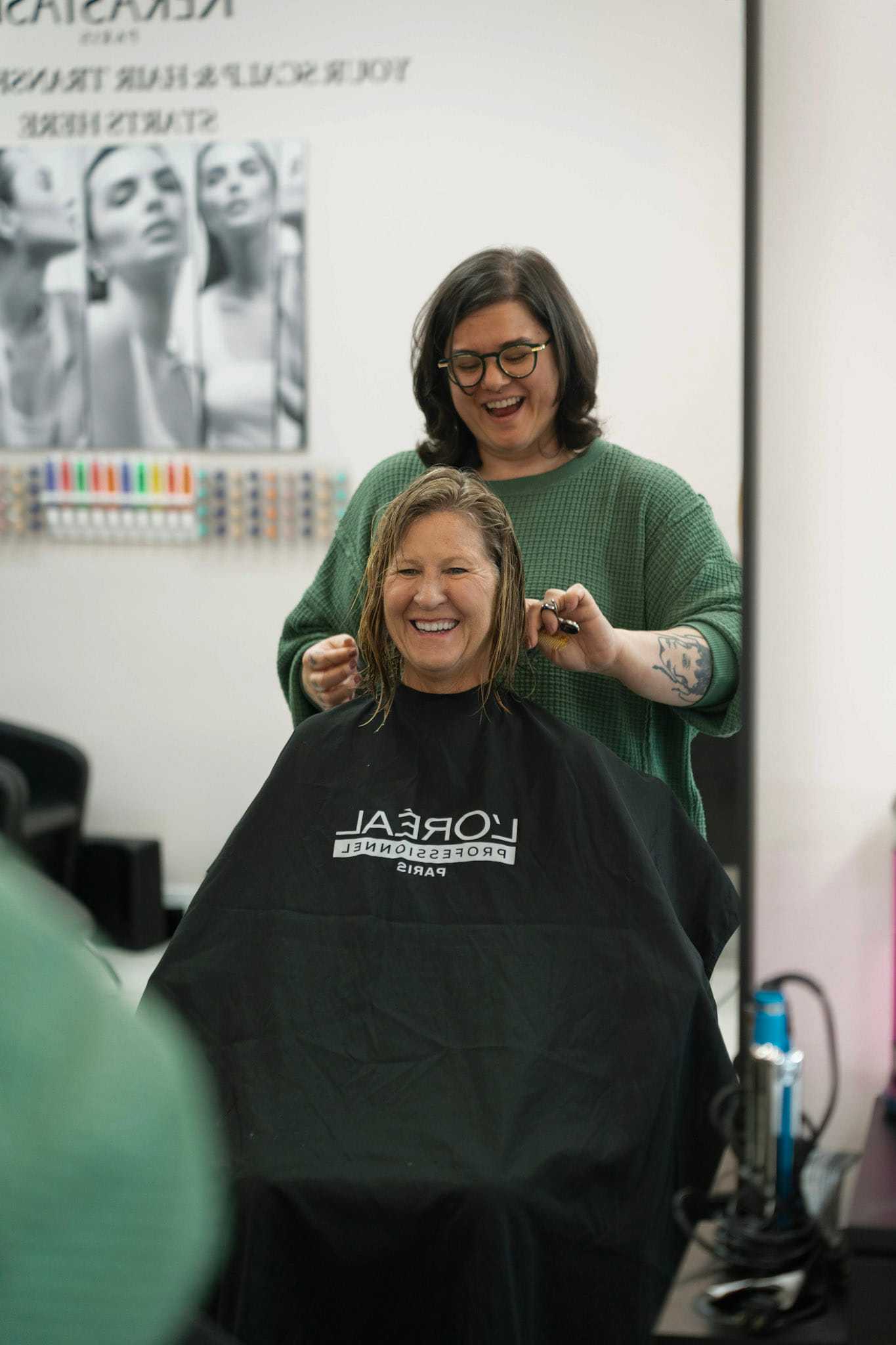Smiling woman gets a haircut in a salon, stylist standing behind.