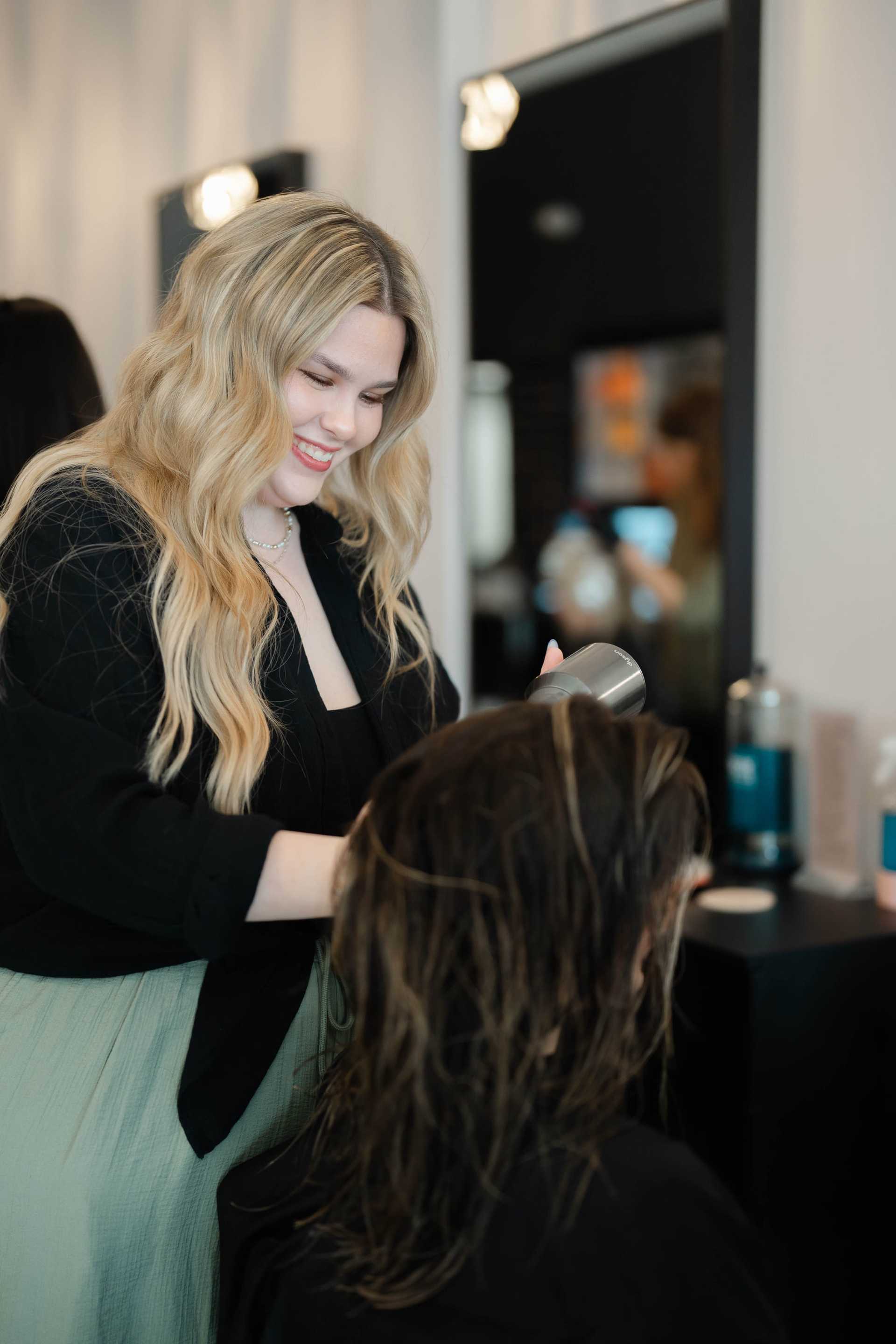 Hairdresser blow-drying a client's hair at a salon.