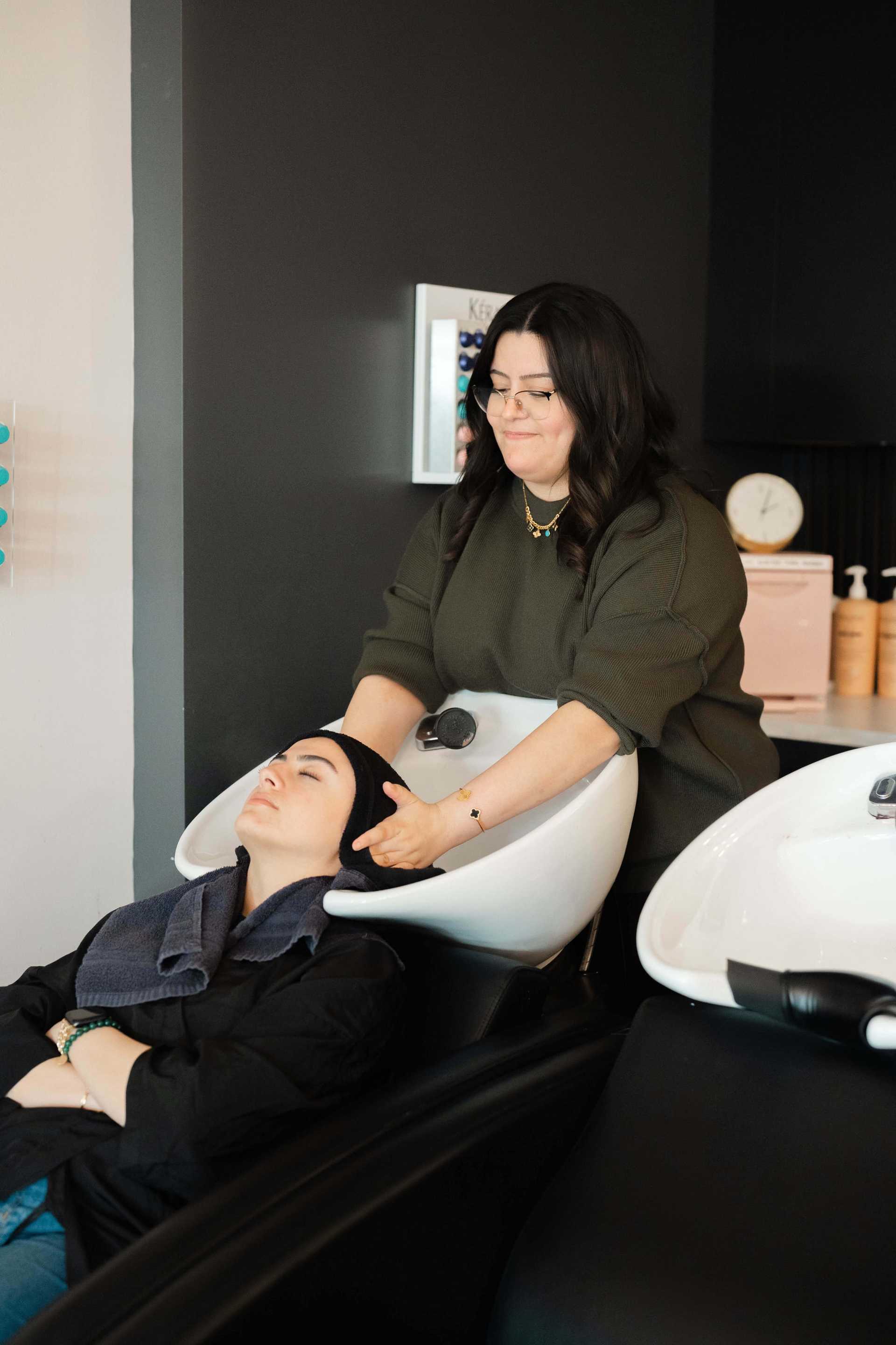 Woman relaxing with hair wash at a salon, attendant gently washing her hair.