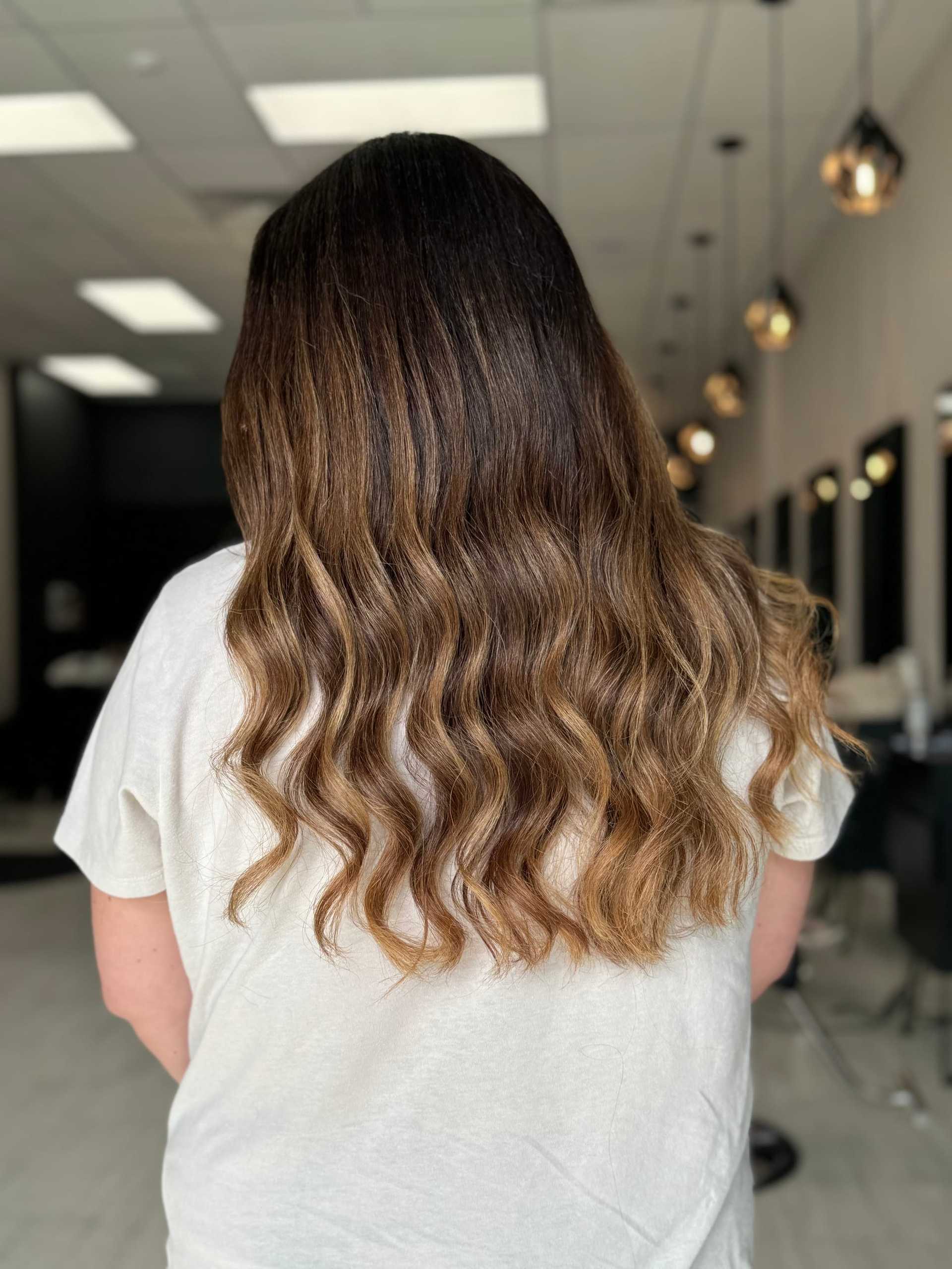 Long, wavy hair with brown and blonde highlights in a modern salon setting.
