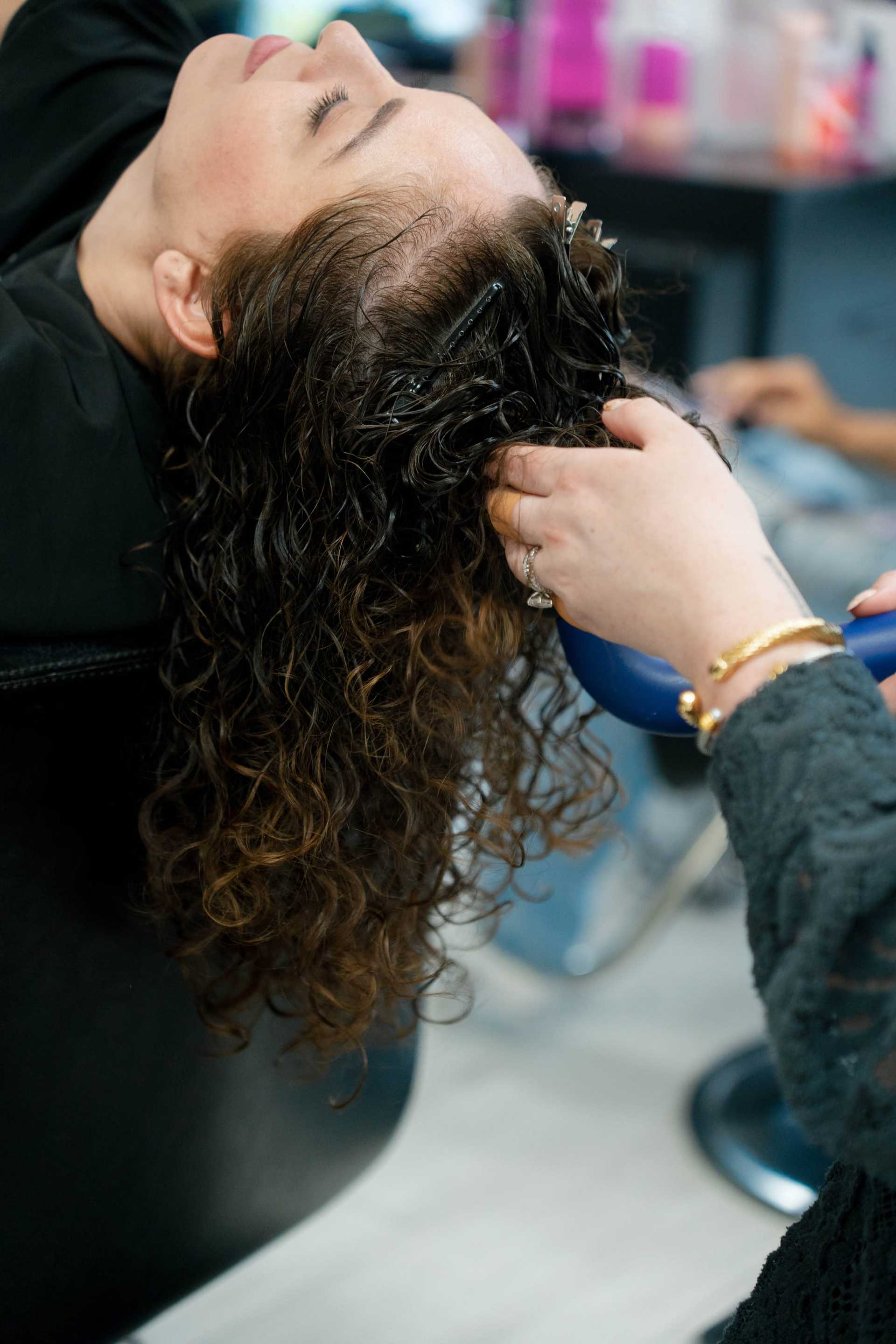 Stylist washing woman's curly hair in salon sink, emphasizing relaxation and care.