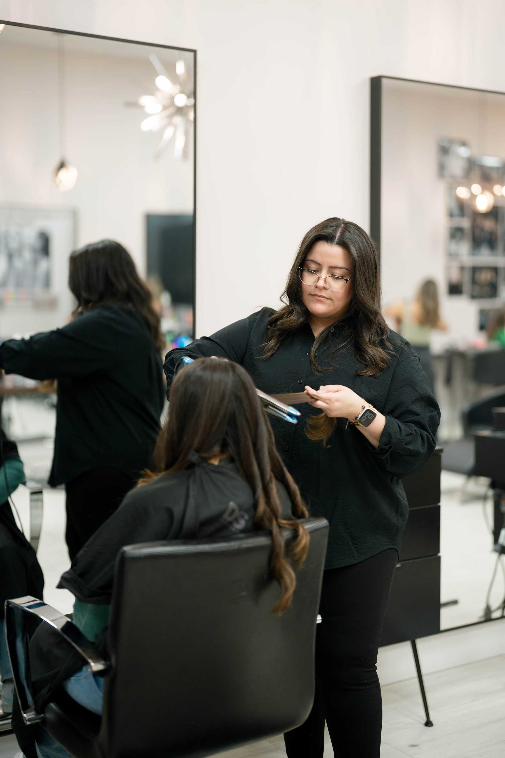 Hair stylist working on a client's long hair in a modern salon.