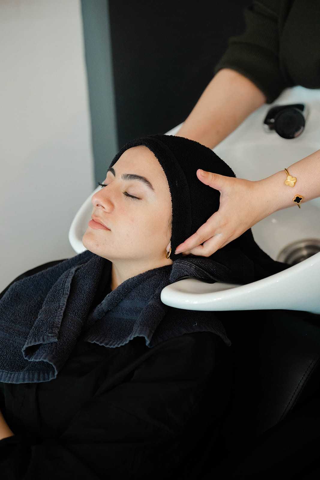 Woman at salon, eyes closed, receiving a relaxing hair wash from a stylist.